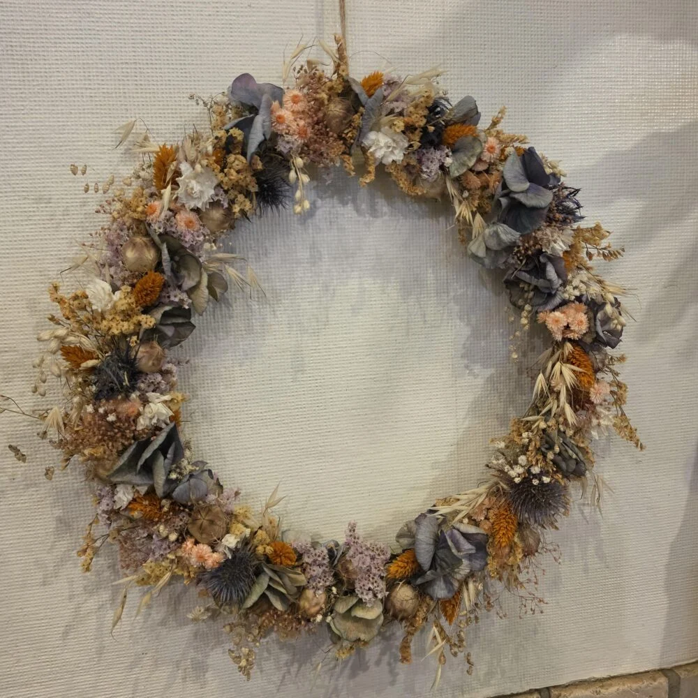 Couronne de fleurs séchées aux tons orangés et bleu-gris, accrochée au mur
