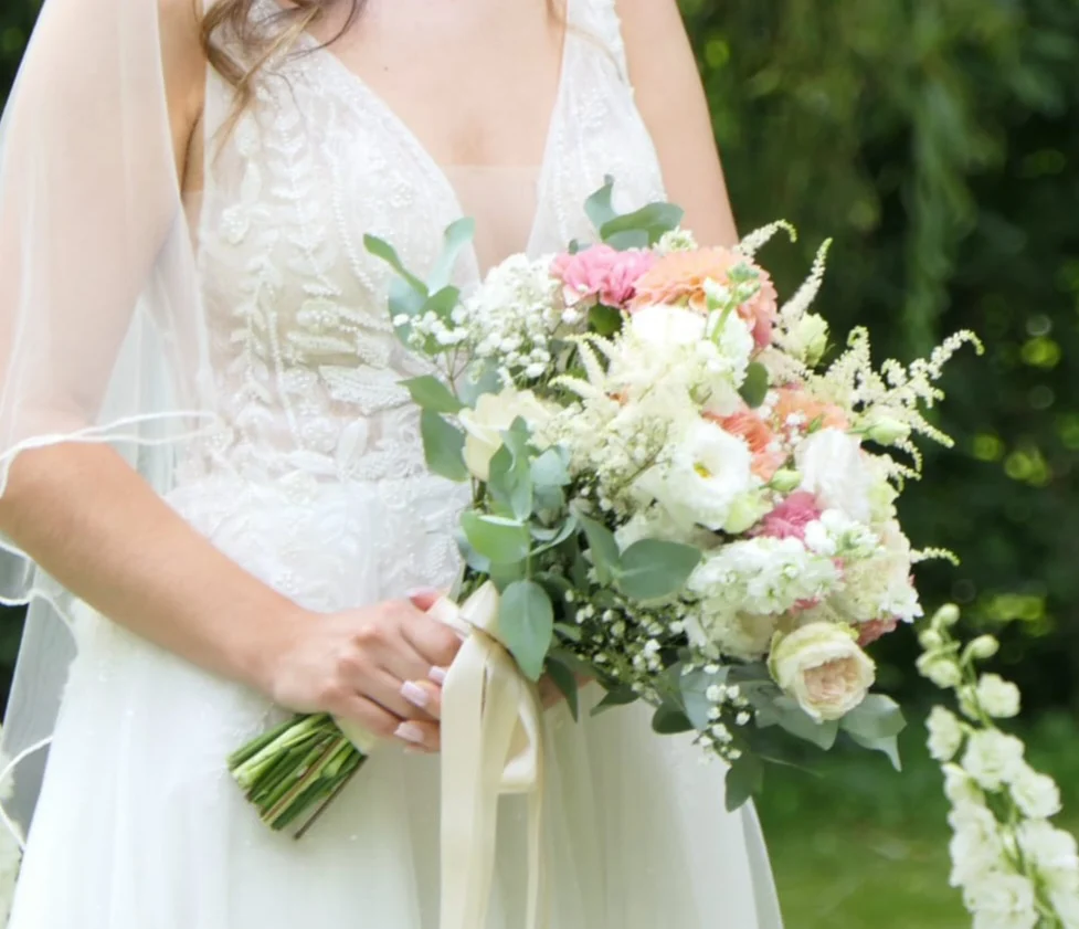 Mariée tenant son bouquet de fleurs blanches et rose pâle, noué de longs rubans
